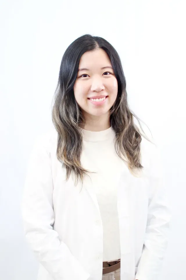 Dr. Sarah Jeon, DDS, wearing a white coat and light-colored top, with long wavy hair and a warm smile, standing against a plain white background - Puyallup Dentist Dr. Sarah Jeon, DDS, wearing a white coat and light-colored top, with long wavy hair and a warm smile, standing against a plain white background - Puyallup Dentist