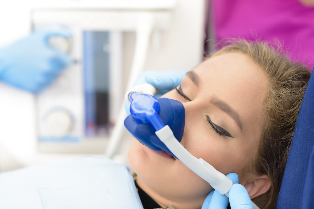 A patient receiving nitrous oxide sedation through a blue mask during a dental procedure - Puyallup Dentist A patient receiving nitrous oxide sedation through a blue mask during a dental procedure - Puyallup Dentist